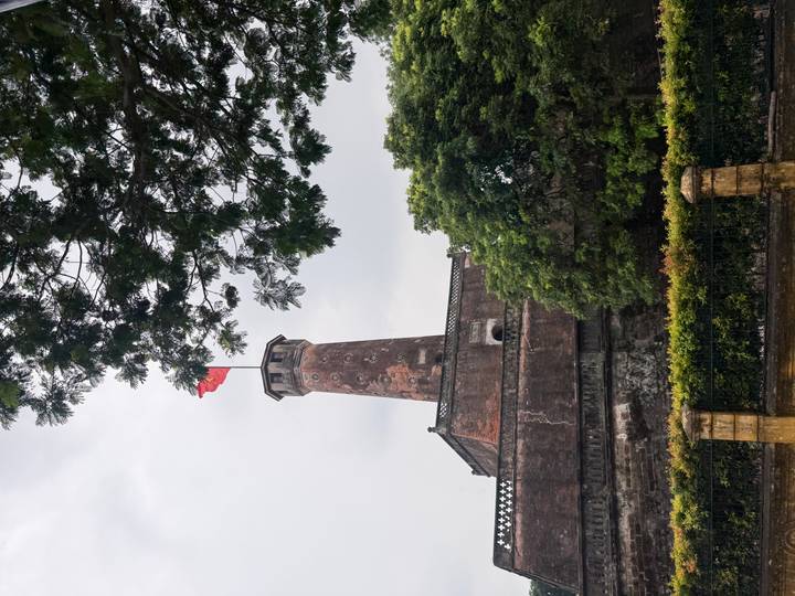 Historic Hanoi Flag Tower with Vietnamese flag flying, framed by tree branches.