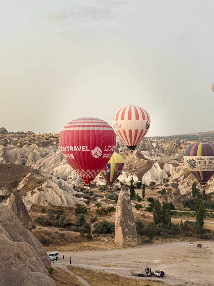 Colorful hot-air balloons drift over Cappadocia's unique rock formations in soft morning light.