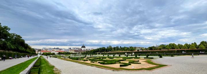 Formal hedged parterres of Vienna’s Belvedere Gardens stretch toward the distant city skyline under a moody sky.