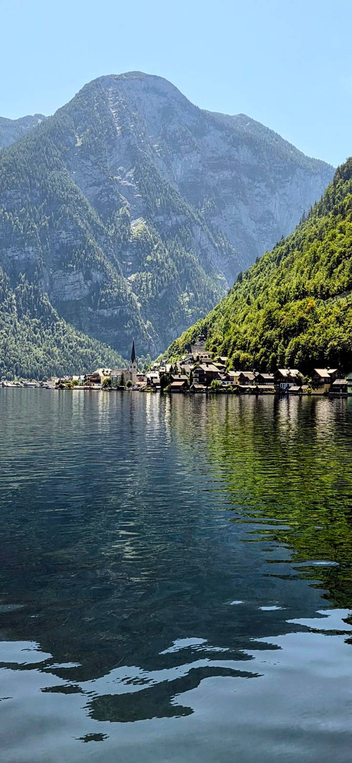 Picturesque lakeside village of Hallstatt with church spire reflected in calm alpine waters.