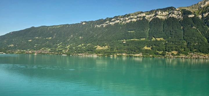 Still turquoise lake bordered by steep forested mountains in Switzerland’s Bernese Oberland.