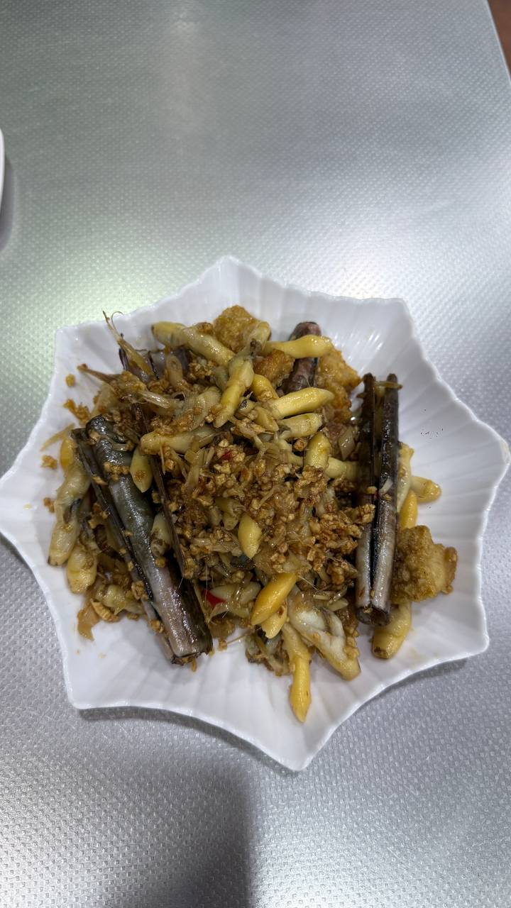 Garlic stir-fried razor clams served in a white scalloped dish.