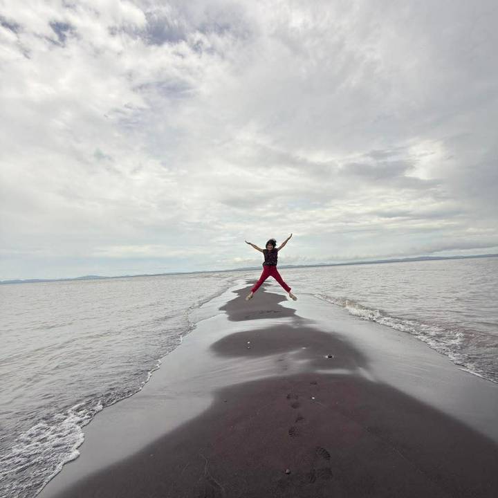 Traveler jumps joyfully on a narrow sandbar stretching into a vast lake or sea.