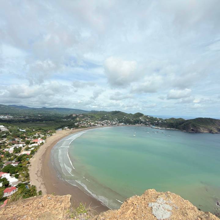 Aerial panorama of crescent-shaped bay, town and green hills of San Juan del Sur.
