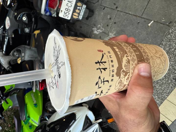 Hand holding a cup of Taiwanese bubble tea on a scooter-lined city street.
