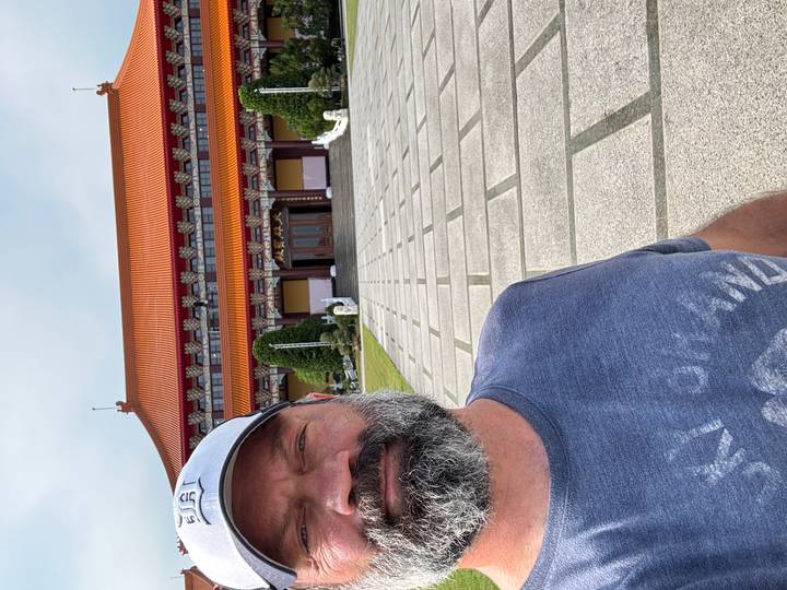 Man takes selfie in front of ornate Buddhist temple with orange tiled roof.