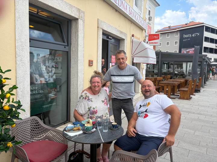 Travelers share coffee and pastries at an outdoor café with a friendly local waiter.