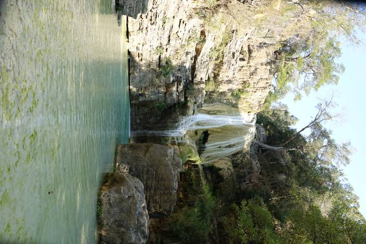 Serene waterfall cascades over rock ledges into a turquoise pool surrounded by green trees.