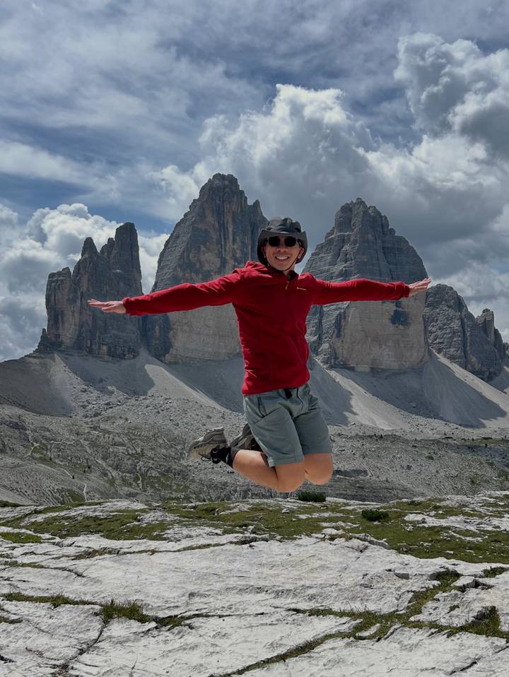 Traveller leaps mid-air with arms outstretched before the towering rock spires of Tre Cime.