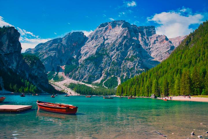 Emerald waters of Lake Braies reflect towering Dolomite cliffs; wooden rowboats float gently in the foreground.