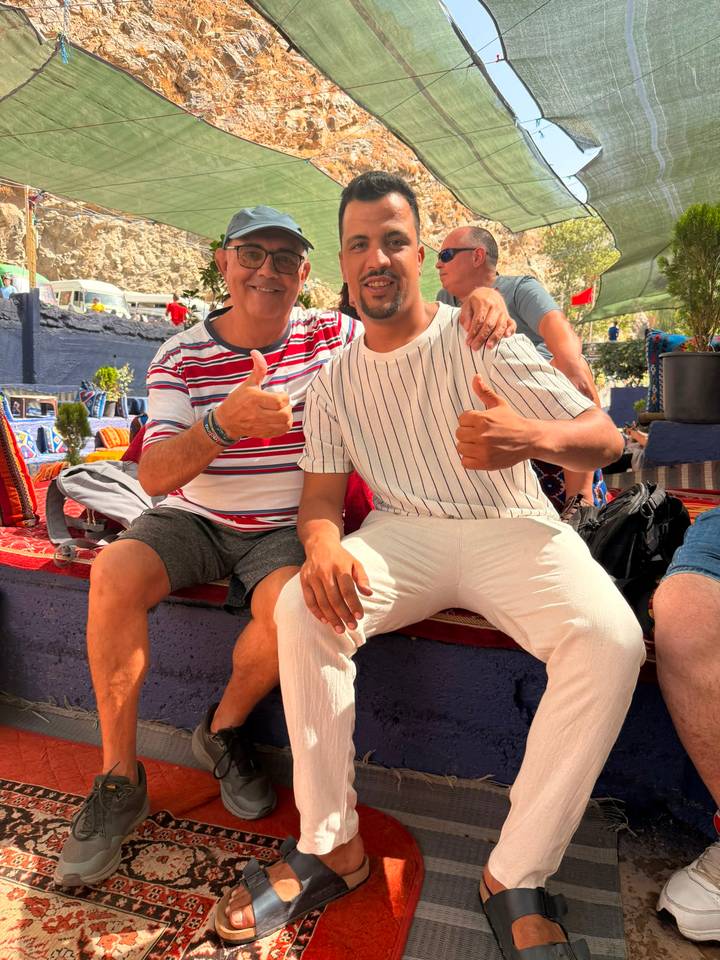 Two men sitting on colourful cushions giving thumbs up in an outdoor café.