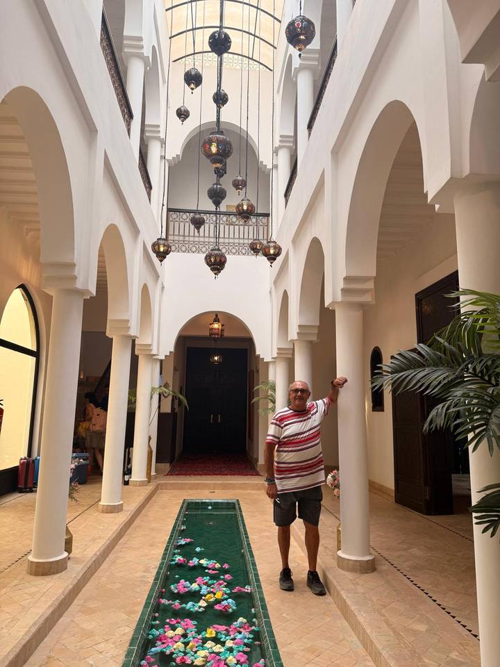 A man poses in the arched hallway of a traditional Moroccan riad with hanging lanterns.