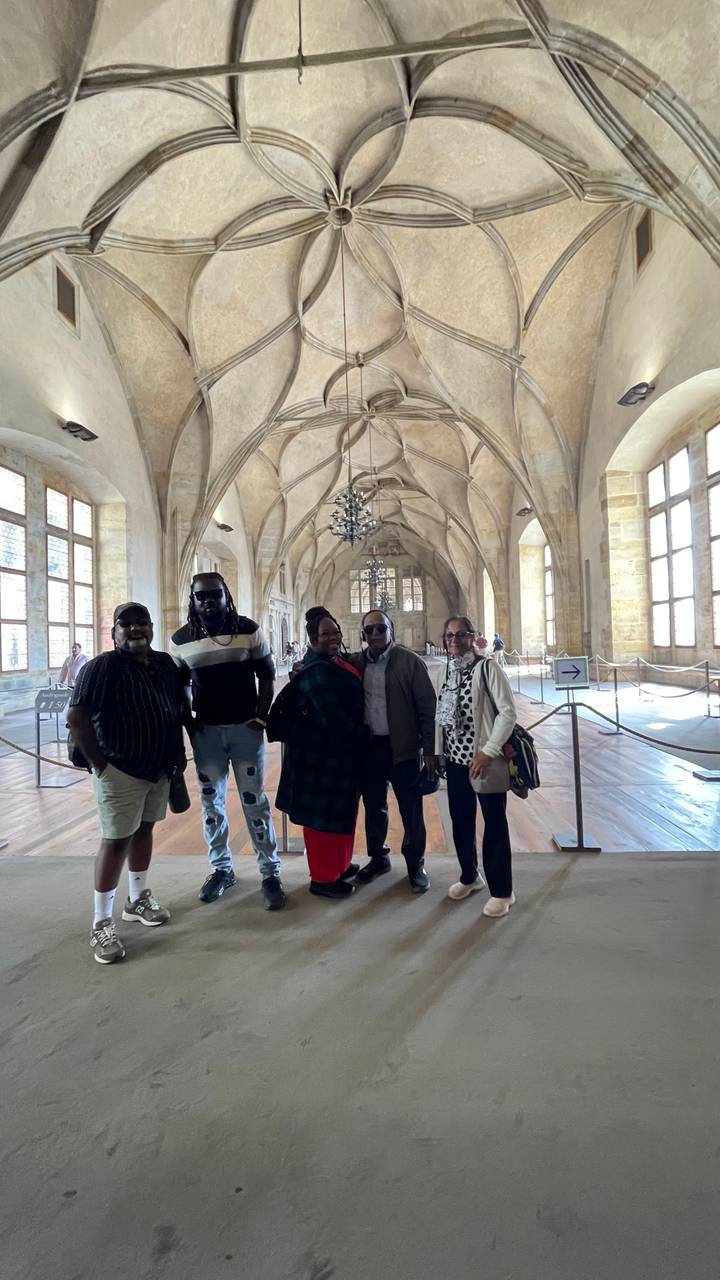 Travellers standing inside a grand vaulted stone hall with chandeliers and gothic windows.