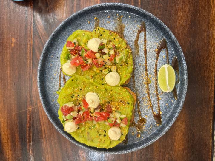 Colourful plate of avocado toast topped with diced tomato, sesame and lime wedge.