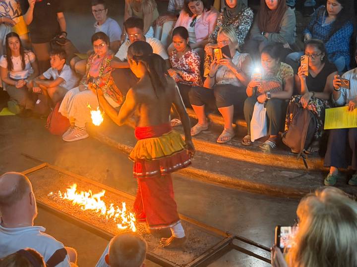 Bare-chested performer walking over flames during a traditional Sri Lankan fire dance while audience looks on