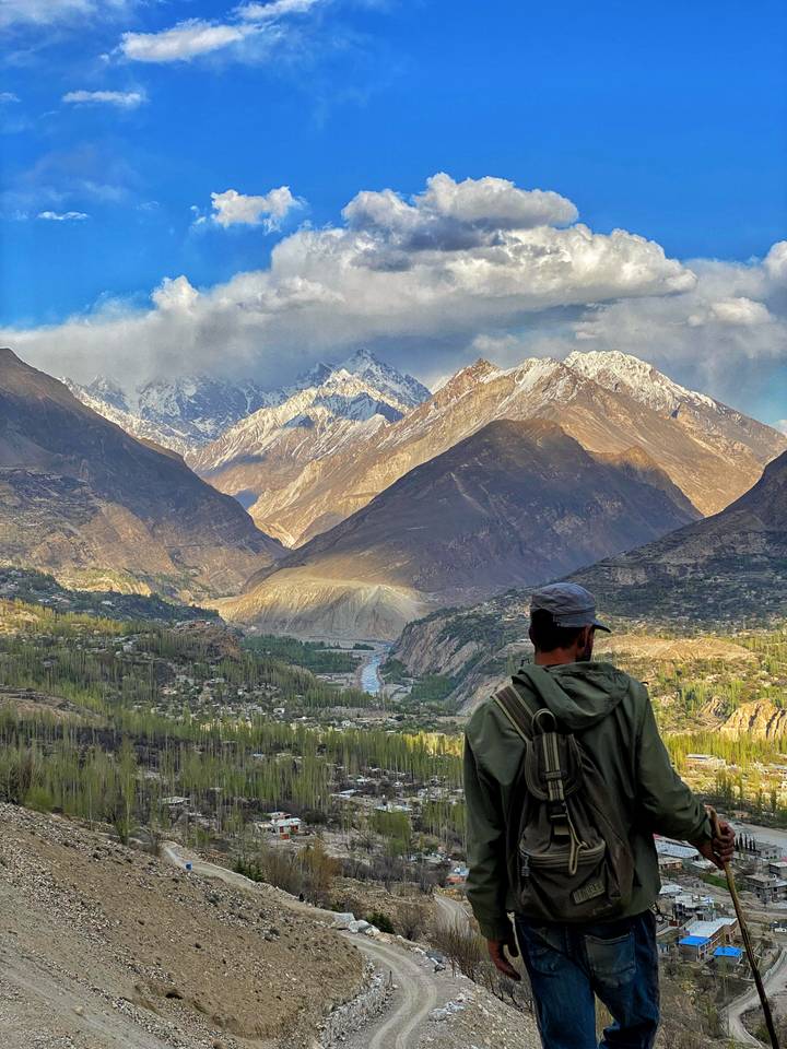 Back view of traveller looking over dramatic snow-capped peaks and deep valley at sunset light.