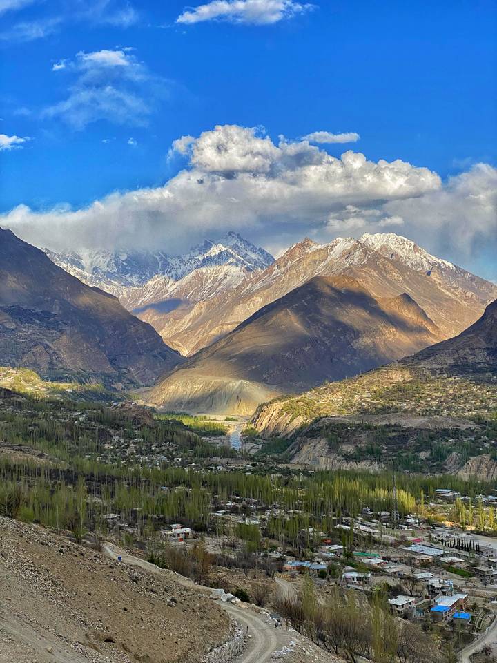 Expansive mountain panorama with rugged peaks dusted in snow and a broad valley below under dramatic clouds.