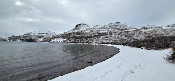 Quiet snowy shoreline curving around a still lake beneath overcast winter skies.