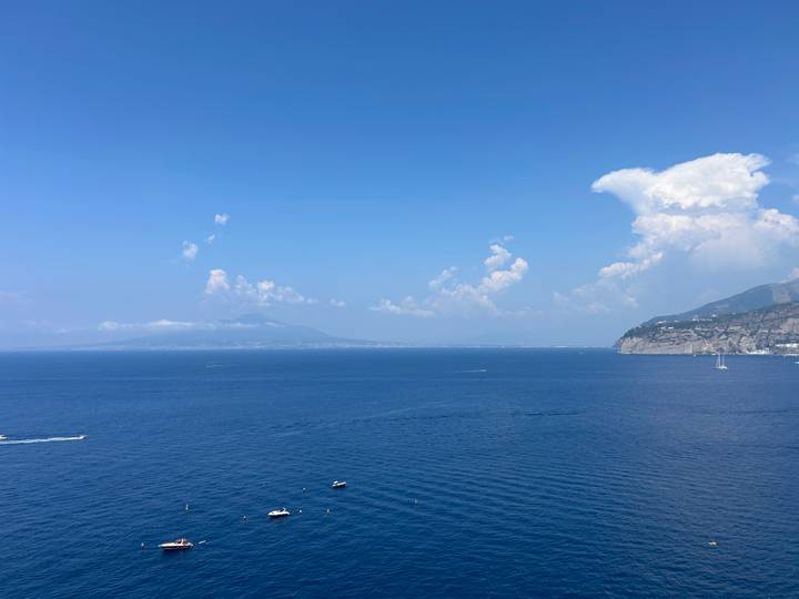 Expansive view over the Bay of Naples with Mount Vesuvius faintly visible on a hazy summer day.