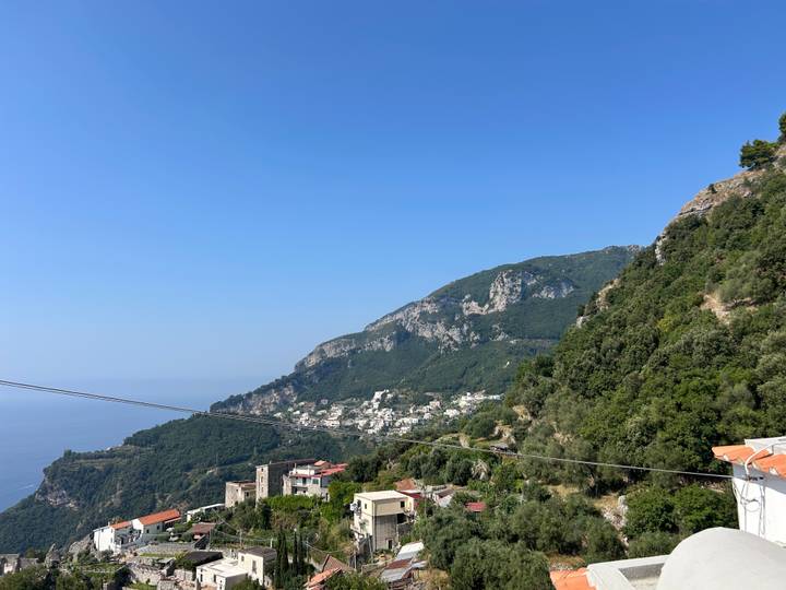 Green hills dotted with small villages descending toward the Amalfi Coast under a clear sky.