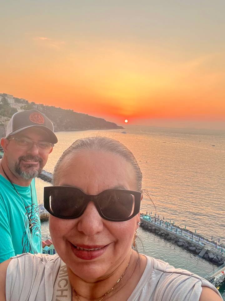 Sunset selfie of couple with orange sky and calm sea horizon in background
