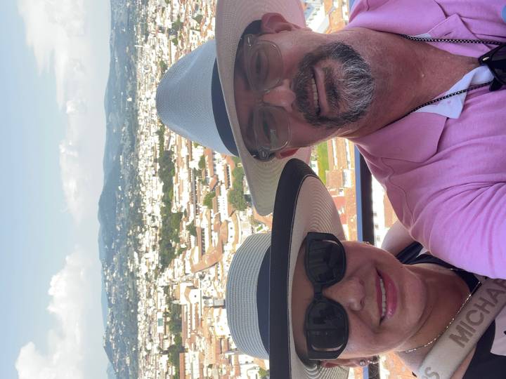 Vertical selfie of couple in sunhats with panoramic city view behind them