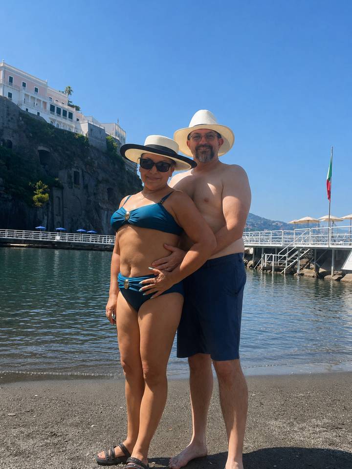 Couple in swimwear posing on waterfront platform with rocky cliffs and calm bay