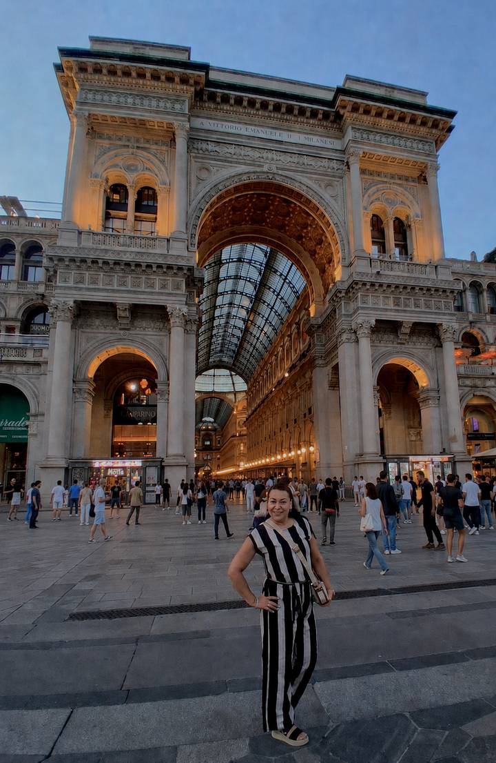 Woman standing inside the illuminated Galleria Vittorio Emanuele II with crowds in background