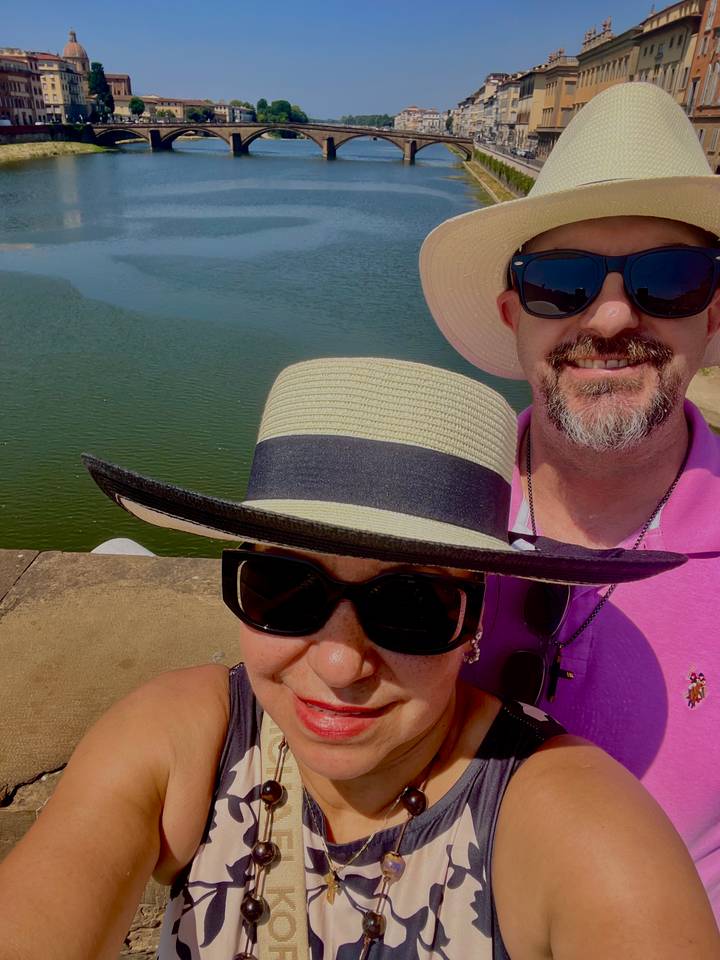 Close selfie of couple wearing hats with water surface behind, faces partly cropped