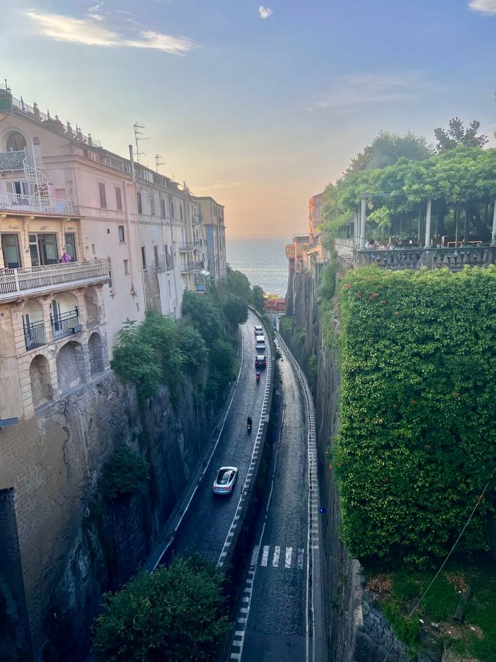 Deep ravine with narrow road descending toward sea between historic buildings at sunset