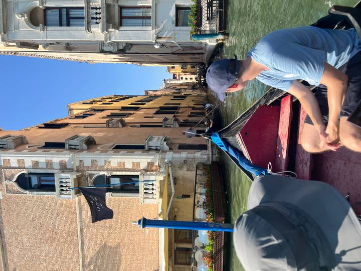Man sitting in gondola turning back as it glides through narrow Venetian canal
