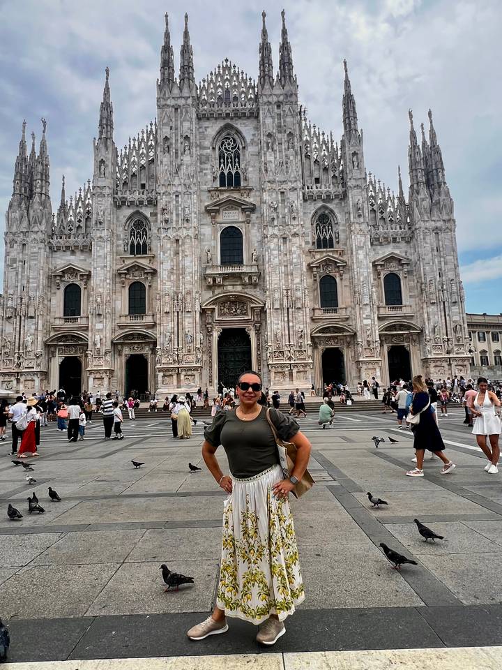 A smiling traveler poses in front of the ornate marble façade of Milan’s Duomo while other visitors wander the square.