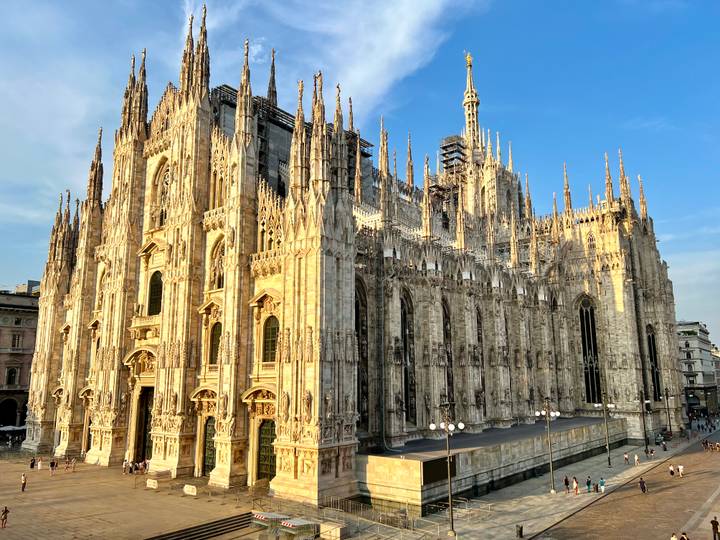 Golden-hour light bathes the intricate spires and flying buttresses of Milan Cathedral against a clear blue sky.
