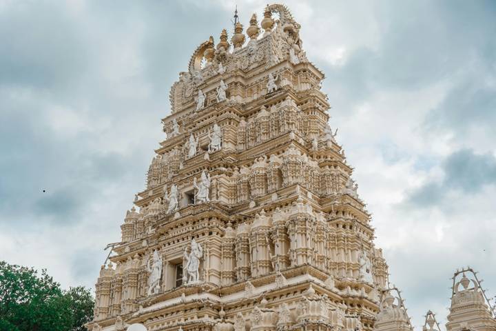 Elaborate white gopuram of a South Indian temple rises into a cloudy sky.