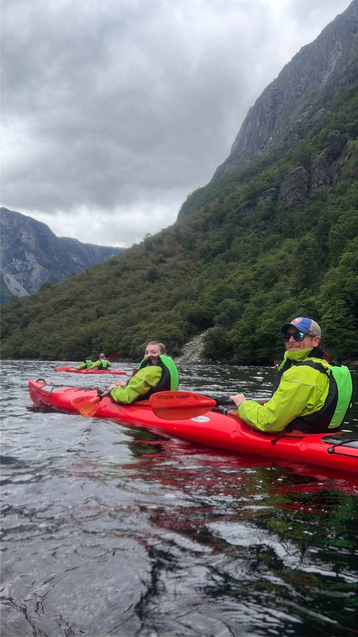 Kayakers in bright jackets paddling on a calm fjord surrounded by steep green mountains