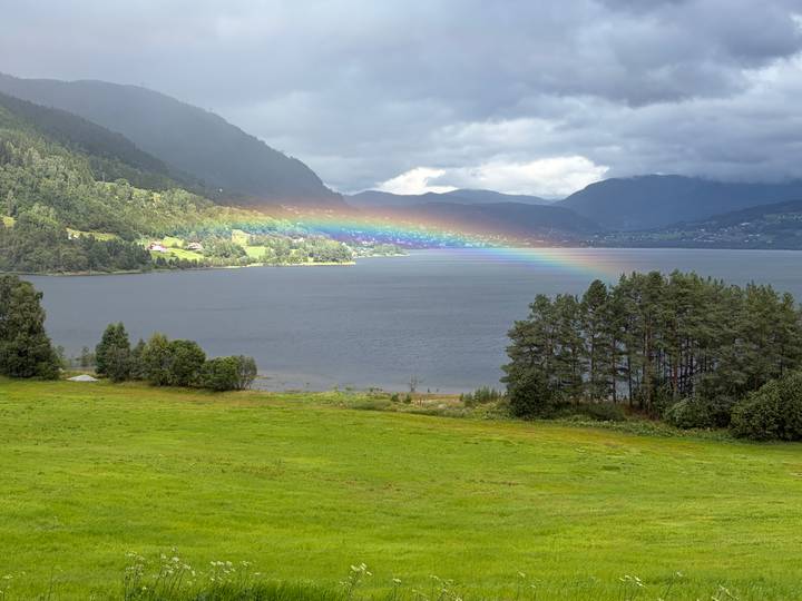 Scenic fjord landscape with vivid rainbow stretching over water between green valleys