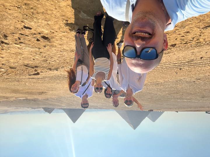 Group selfie on the desert plateau with three great pyramids rising behind them under bright sun.