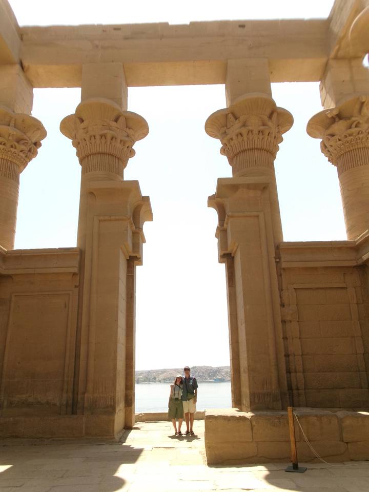 Upward view between two sandstone columns of an ancient temple against an overexposed bright sky.