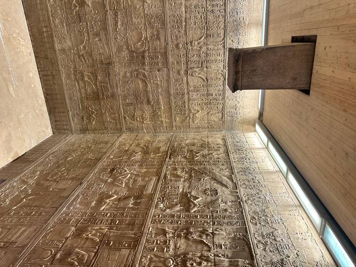 Dimly lit chamber covered in intricate hieroglyphic reliefs with a stone pedestal in the center.