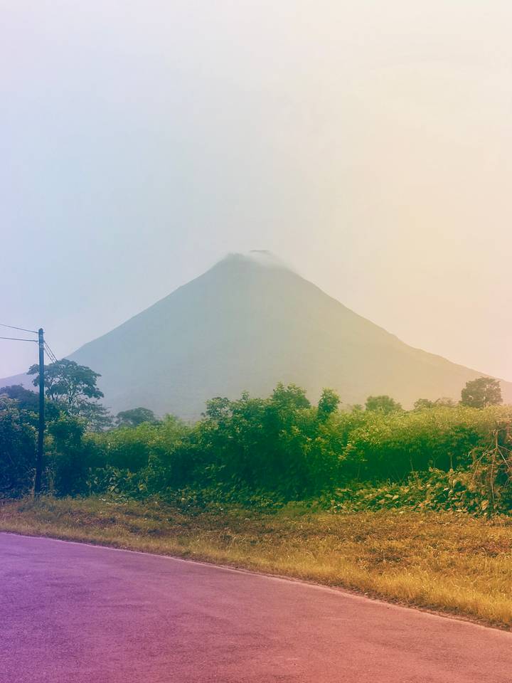 A mist-shrouded volcanic cone rises behind lush tropical vegetation