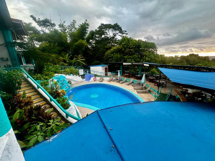 Outdoor hotel pool area surrounded by lush plants under a moody evening sky
