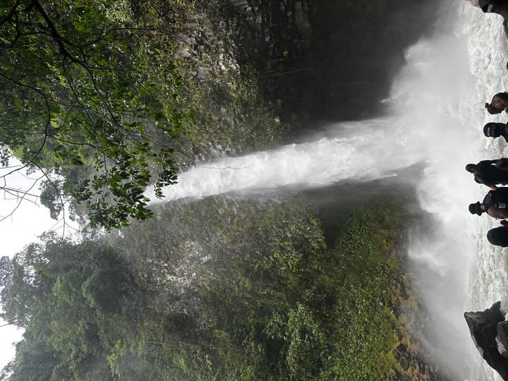 Tall jungle waterfall crashing into a pool where visitors gather at the base