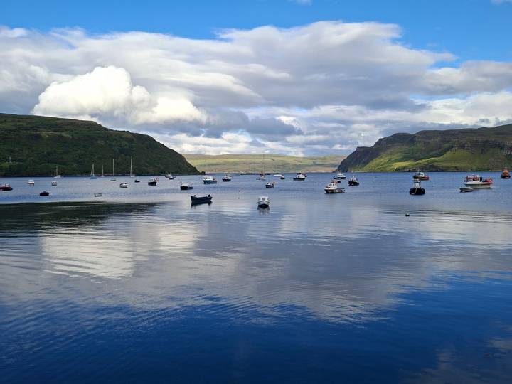 Calm harbour filled with small boats under bright clouds and rolling hills