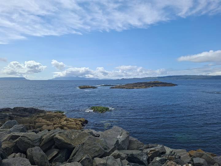 Bright blue sea with rocky islets and distant cloud-topped mountains