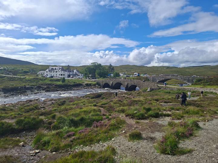 Historic stone bridge over a rocky river with travellers exploring the scenic moorland
