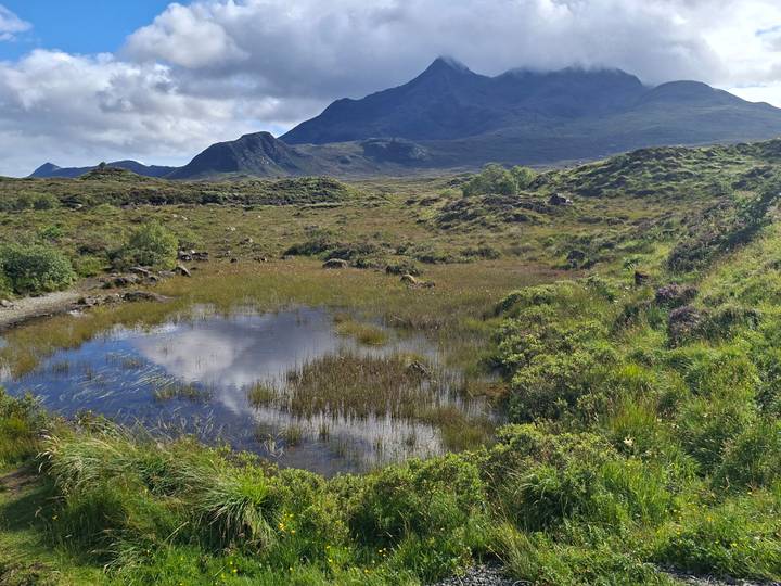 Wide moorland with small pond reflecting clouds and rugged mountains in background