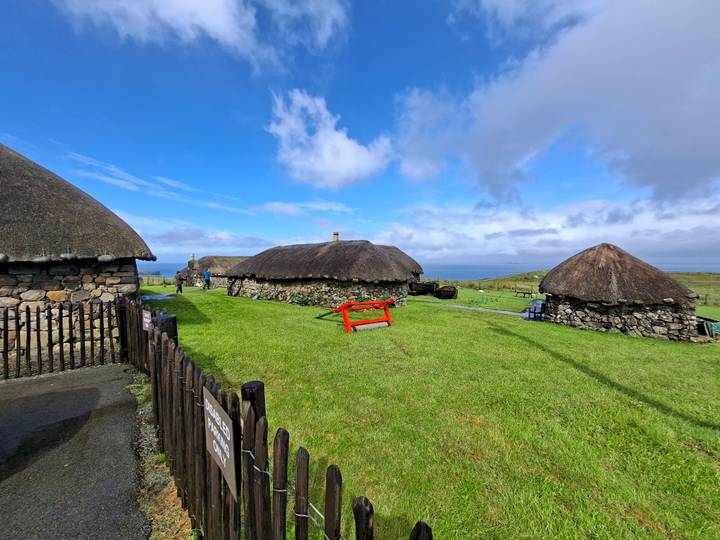 Traditional thatched stone cottages in an open-air museum against a bright sky