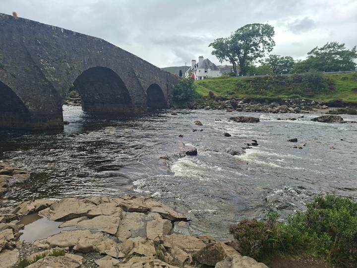 Stone arch bridge crossing a fast river with countryside inn beyond