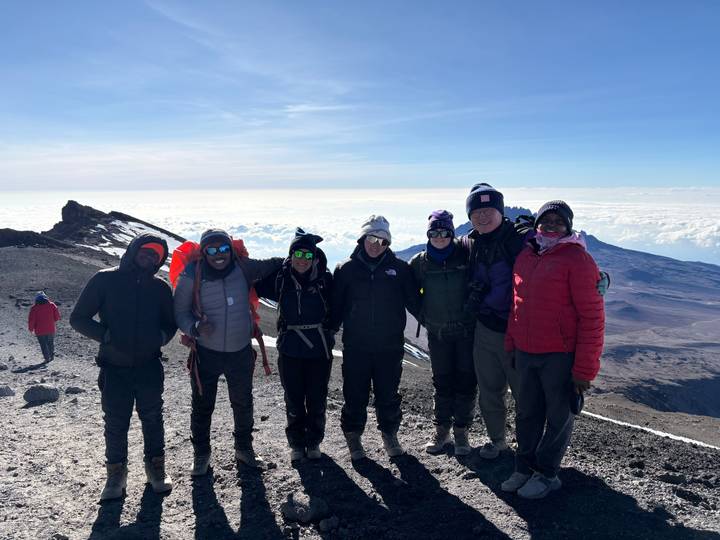 Summit group bundled in winter gear atop Mount Kilimanjaro with sea of clouds and crater ridge behind