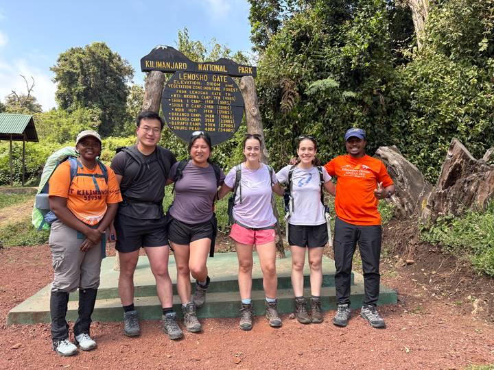 Trekking team posing at Lemosho Gate sign in Kilimanjaro National Park surrounded by forest greenery